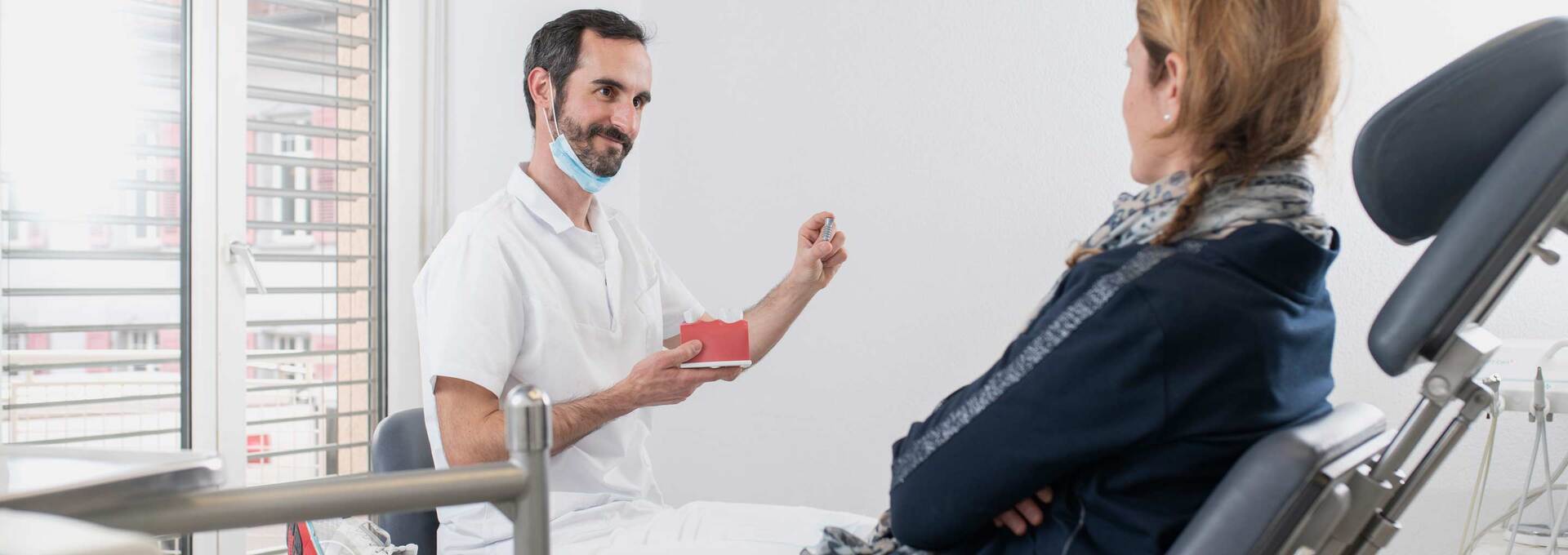 Zahnarzt zeigt Patientin ein Zahnimplantat Zahnarzt zeigt Patientin ein Zahnimplantat